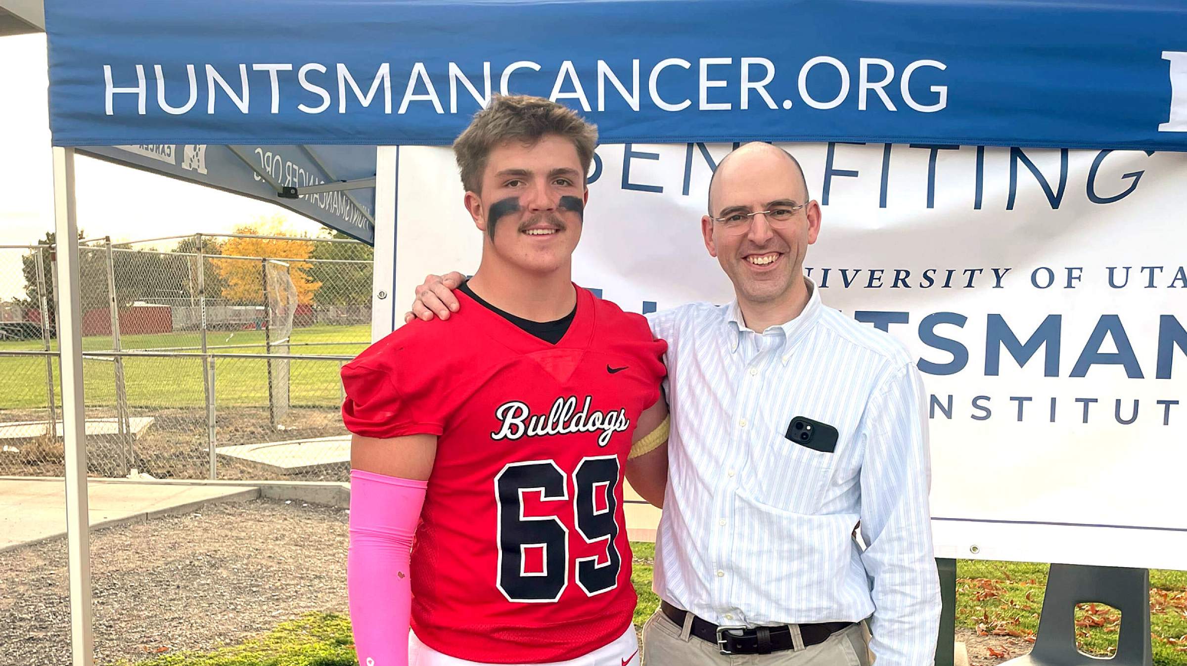 Gunner standing with Dr. Jones at the Huntsman Cancer Institute table at the senior night football game