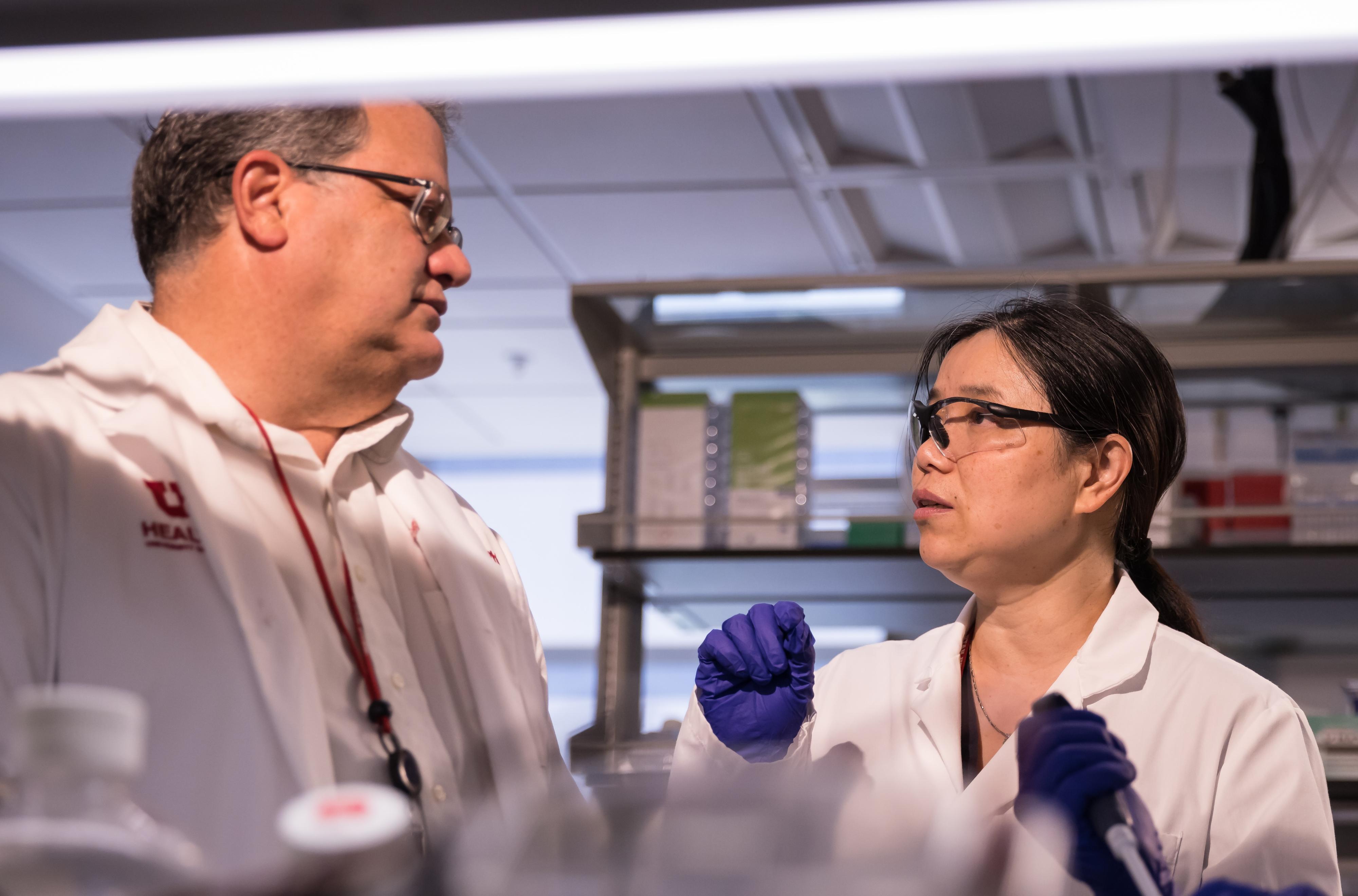 Two people in white coats converse animatedly in a dimly lit lab.